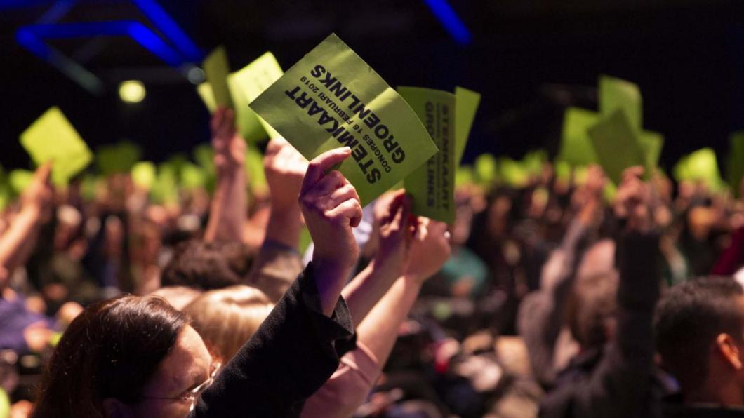 GroenLinks leden stemmen tijdens een congres met een stemkaart boven hun hoofd.