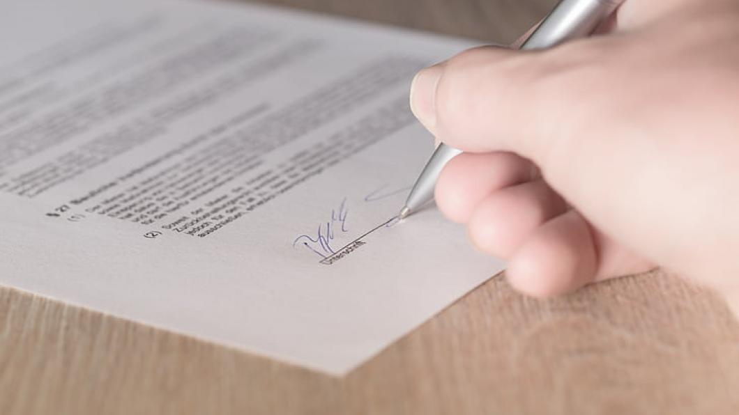 Een hand ondertekent een document.